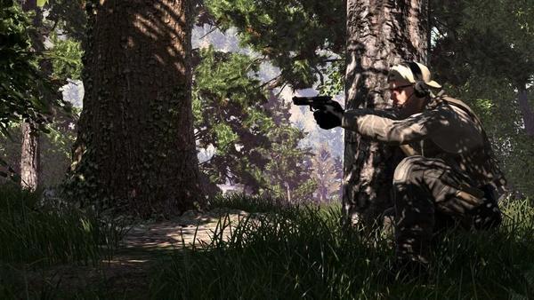 Un soldato in tenuta tattica accucciato dietro un albero in un bosco, mentre mira con una pistola nel videogioco Ground Branch