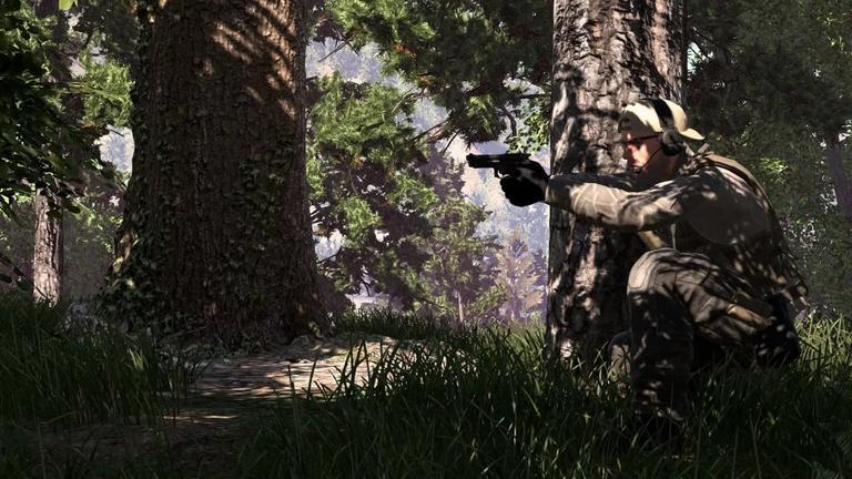 Un soldato in tenuta tattica accucciato dietro un albero in un bosco, mentre mira con una pistola nel videogioco Ground Branch